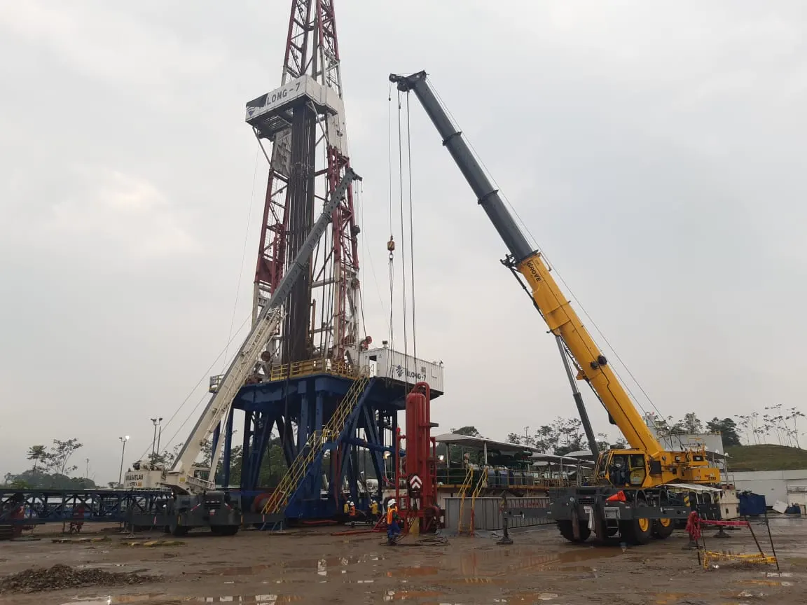 Grúa móvil realizando una maniobra de izaje junto a un equipo de perforación en una locación petrolera